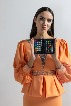 Playful model pouting while holding color chart in orange dress