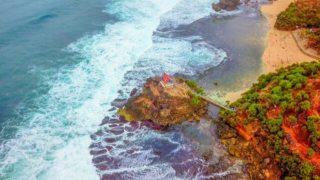 Aerial view of Kukup Beach Nature Inn situated along the coastline with rocky cliffs, sandy beach, and turquoise ocean waters in Kecamatan Tanjungsari, Daerah Istimewa Yogya, Indonesia.