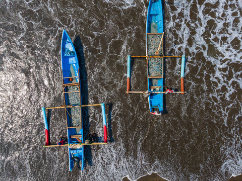 Aerial view of two blue outrigger fishing boats with fishermen on board navigating the surf near the shore in Cilacap, Central Java, Indonesia.