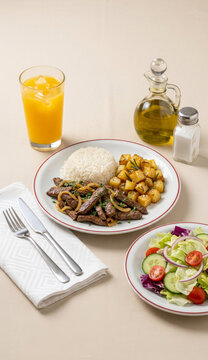Traditional meal featuring strips of liver with onions, accompanied by white rice, roasted potatoes, mixed salad, and a glass of orange juice with ice cubes - f&iacute;gado bovino acebolado