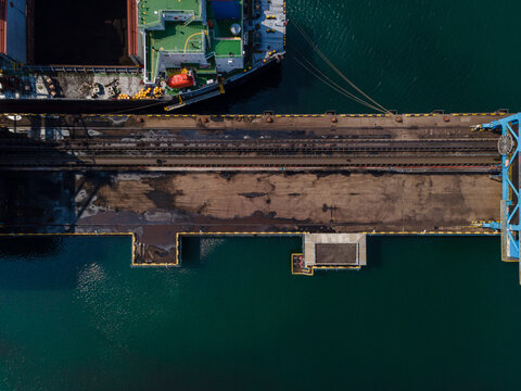 Aerial view of a large cargo ship docked at the industrial port terminal with rail tracks and loading equipment in Cilacap, Central Java, Indonesia.