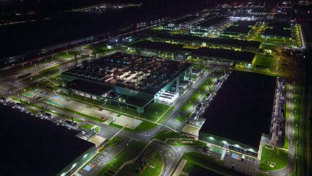 Aerial view of a large data center illuminated at night with surrounding parking lots and access roads in the Netherlands.