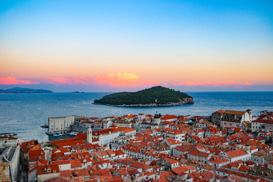View of the historic walled city with its iconic red-tiled rooftops, ancient stone fortifications, and the Adriatic Sea at sunset, Dubrovnik, Croatia.