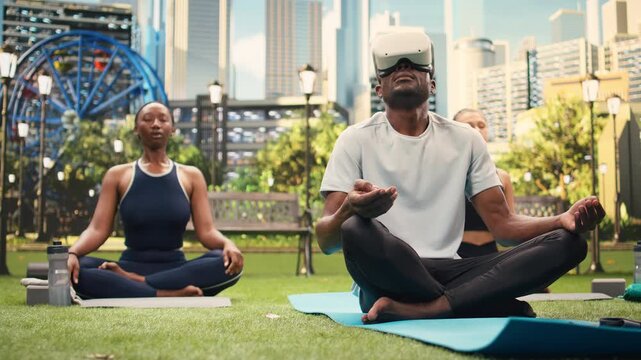 Yoga participant with virtual reality glasses sits cross-legged on mats in public park, starting outdoor meditation and deep breathing in lotus position during an immersive VR Pilates practice.