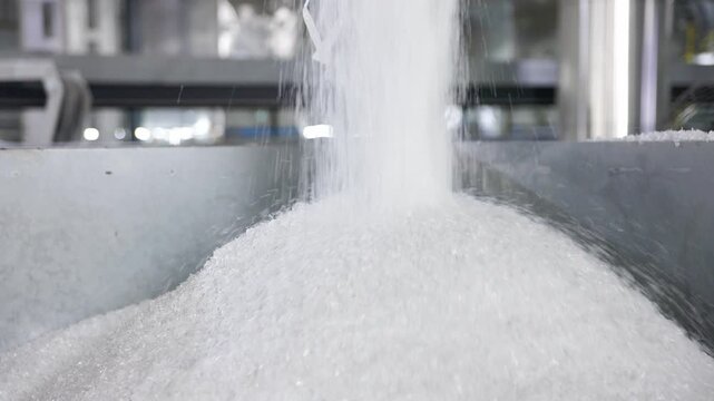 Automated machine pours granulated sugar into a container in a modern factory.