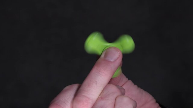 A close-up view of a green fidget spinner spinning on a finger, highlighting the smooth motion and balance as it rotates, with a dark background enhancing the visual focus on the spinner