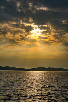 View of the sun setting over the Adriatic Sea with dramatic golden clouds and silhouettes of distant hills near Hvar, Split-Dalmatia County, Croatia.
