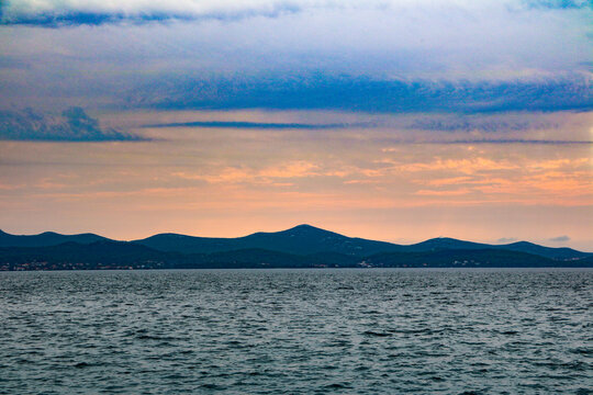 View of the coastline of Hvar island at sunset with rolling hills and calm sea under a cloudy sky in Hvar, Split-Dalmatia County, Croatia.