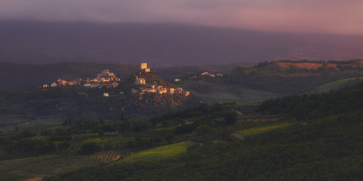 View of a hilltop village surrounded by rolling hills, vineyards, and olive groves in Tuscany, Italy.
