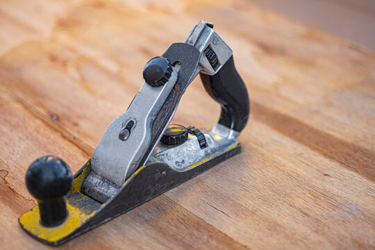 Hand plane on a workbench. A worn metal block plane with black knobs sits on a wooden surface, blade assembly raised. Ideal for woodworking, DIY, and craft content.