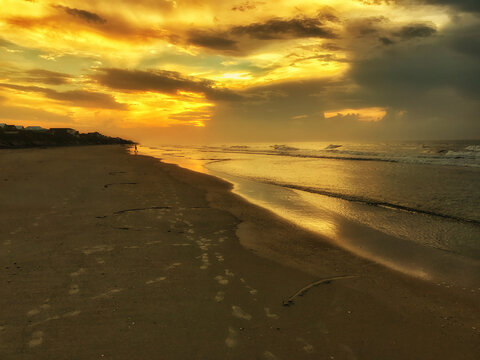 View of the sandy beach at Topsail Island during a golden sunset with footprints in the sand and gentle waves rolling onto the shore in North Topsail Beach, North Carolina, United States.