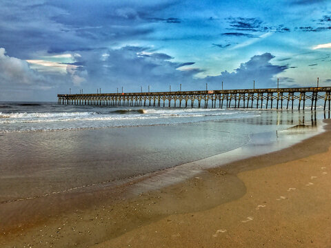 View of Topsail Island pier extending over the Atlantic Ocean under a dramatic cloudy sky at the beach in North Topsail Beach, North Carolina, United States.