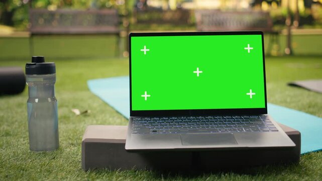 Green screen mockup appears on a laptop beside water bottle and yoga mat, providing replaceable editable display for outdoor wellness content, with empty space for screen replacement.