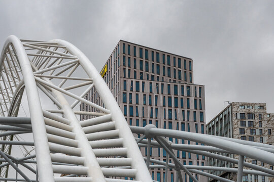 View of the white steel structure of a facade with modern office buildings in the background under a cloudy sky in Rotterdam, South Holland, Netherlands.
