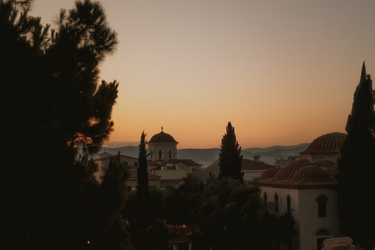 View of a historic church with domes at sunset, framed by cypress trees in Athens, Greece.