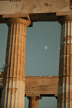 View of the ancient marble columns of the Acropolis framing a crescent moon in the clear sky in Athens, Greece.