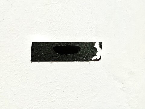 A piece of worn black electrical tape with a tear and a hole stuck on a textured white surface.