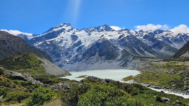 View of Mount Cook and glacier above a turquoise glacial lake, seen from the Hooker Valley track with rocky slopes and alpine vegetation, Mt Cook National Park, Canterbury, New Zealand.