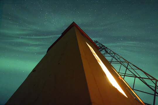 View of Hofn Lighthouse illuminated against the vibrant green aurora borealis in the night sky, Hofn, Sveitarfelagid Hornaf, Iceland.