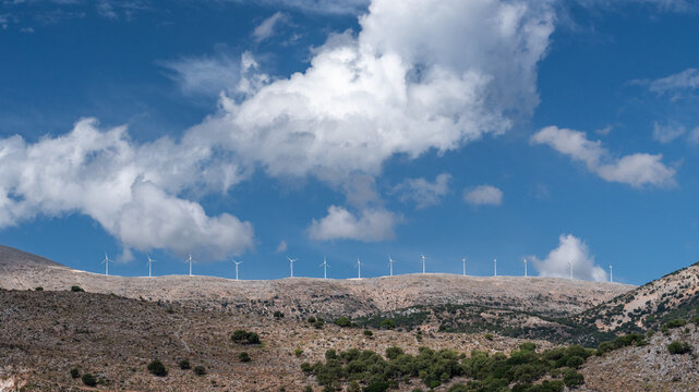 View of wind turbines standing on a rocky ridge under a blue sky with clouds in Argostoli, Greece.