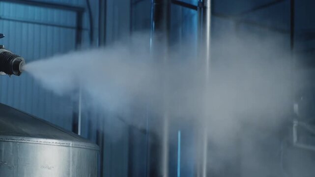 Metallic cryogenic tank nozzle releasing a thick cloud of cold vapor in a dark industrial facility