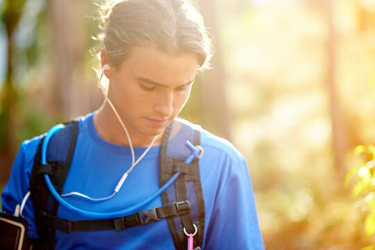 Fitness, man and earphones with music in forest for hiking podcast, cardio playlist and wellness exercise. Space, hiker and listening to audio with backpack for healthy training, workout and trekking
