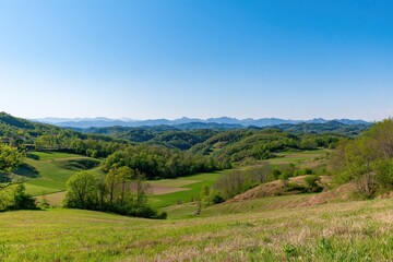Obraz premium Rolling green hills and distant mountains under a clear blue sky