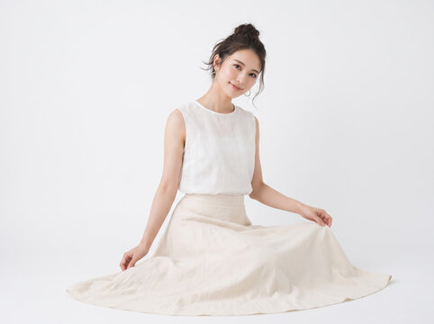 白いノースリーブとベージュのフレアスカートを着て床に座る女性