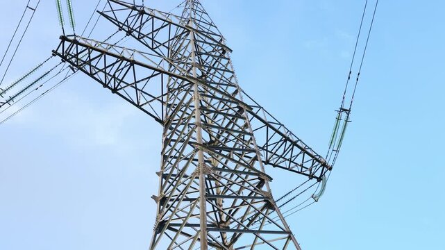 Low angle view of a steel lattice transmission tower supporting multiple overhead power lines and suspended insulators against a clear blue sky
