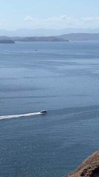 Aerial view of a speed boat cruising across deep blue ocean waters leaving a white wake, with mountain ranges and distant islands under a clear sunny sky.