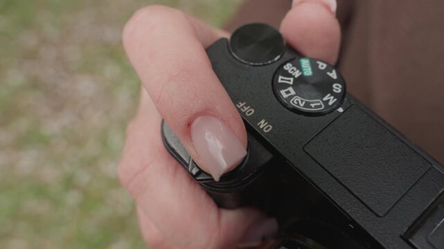 Close up view of hand holding and adjusting shutter button on black digital camera. thumb presses down while index finger remains near focusing on interaction with mode dial visible AUTO SCN