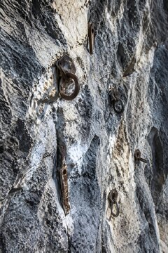 Rocky cliff face studded with climbing anchors rusted pitons and scratched limestone