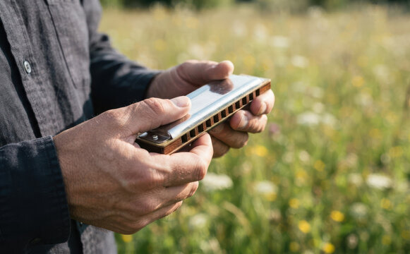Man holding a harmonica outdoors in a natural meadow representing acoustic folk music and lifestyle