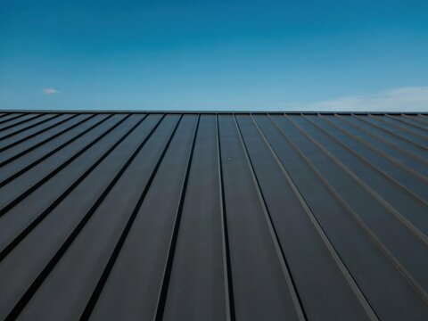 Modern standing seam metal roof panels against clear blue sky reflecting clean lines for residential architectural design.