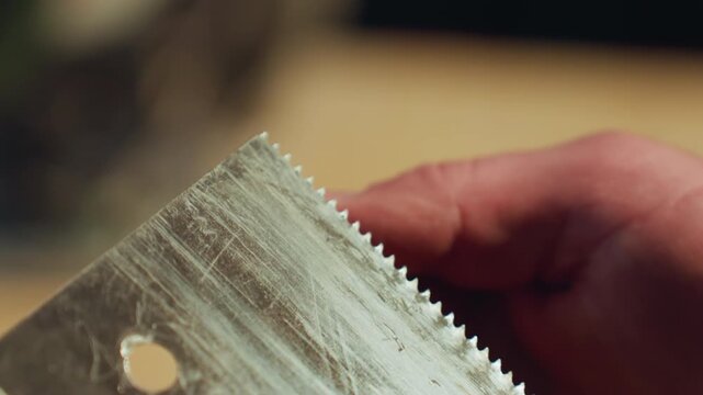 Close up shows hands examining or using old metal saw with visible teeth. focus remains on detailed interaction between hand and sharp worn tool blade