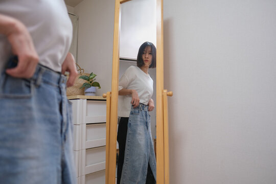 鏡を見ながらジーンズを履こうかどうか迷う女性