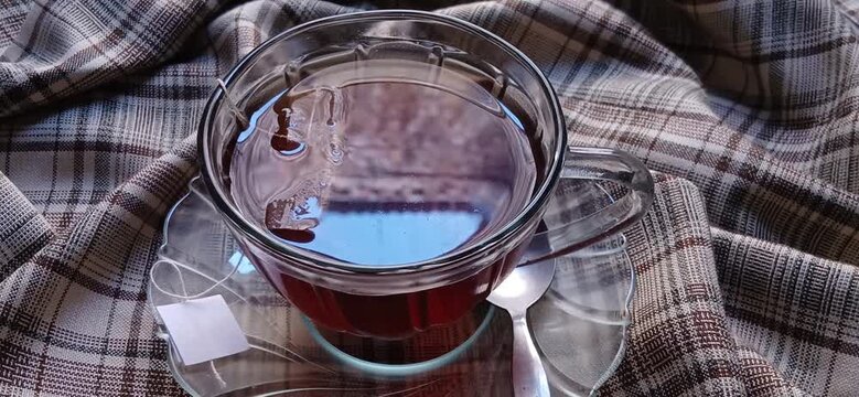 hot and steam black tea with a teabag in a clear glass cup served on a classic plaid cloth, creating a warm and cozy afternoon tea atmosphere