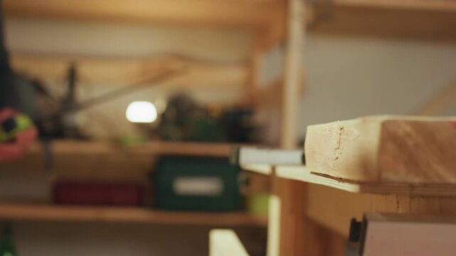 Person works in workshop focusing on precise joinery tasks. green C clamp is used to secure pieces of unfinished light colored wood together with various woodworking tools and materials