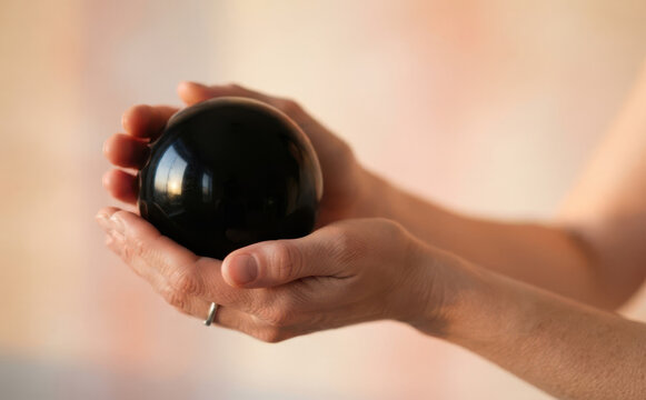 Woman holding a black obsidian crystal sphere in her hands symbolizing divination, magic, and spiritual healing practice