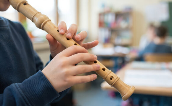 Young schoolboy playing wooden recorder flute instrument in music class classroom