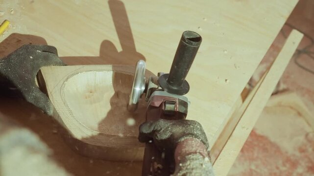 Gloves clad hands guide electric router through precise cuts on shaped wooden stock in well used woodworking shop with sawdust scattering and tools visible