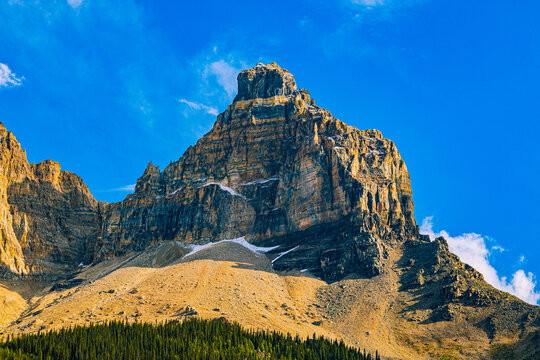 Sunlit rocky summit with lingering snow patches rises against a deep blue sky in Yoho National Park, Canada.