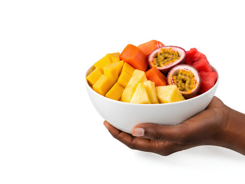 A hand holding a bowl of healthy vegan salad fruits with pineaple, watermelon, dragon fruit, radish isolated on white background. A black hand carrying a bowl of fruit salad