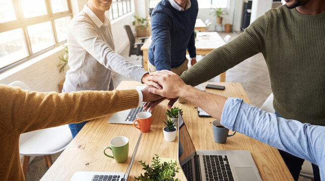 Coworker teamwork around desk with diverse office team joining hands and sharing enthusiasm in bright workplace