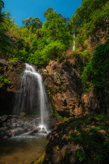 A picture of a waterfall cascading down a high rock cliff in the forest, nature. © Pongsorn