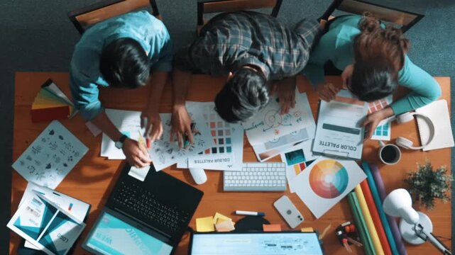 Top down aerial view of project manager looking at screen while designer writing idea. Smart business team explain idea of logo design while designer choose theme while looking at palette. Symposium.