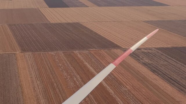 Red and White Wind Turbine Blade Above Parallel Plowed Fields