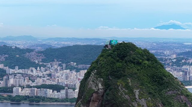 Pao de Acucar rises above the Urca district in Rio de Janeiro, Brazil, with Guanabara Bay and dense buildings behind the peak, slow reveal with orbit movement.