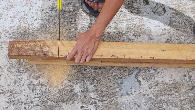 Man completing manual saw cut on wooden board outdoor on concrete surface