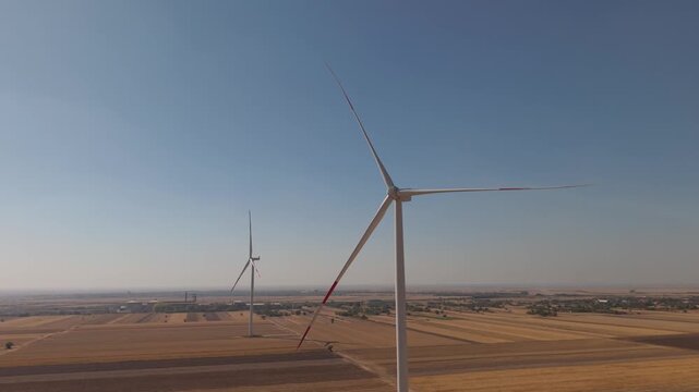 Close Aerial Pass by a Wind Turbine Above Fields and a Rural Settlement